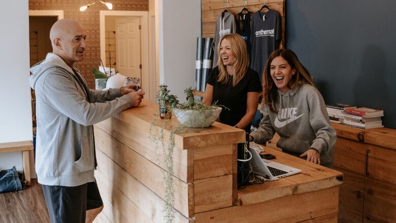 Yogis are seen gathering around the front desk of a yoga studio.