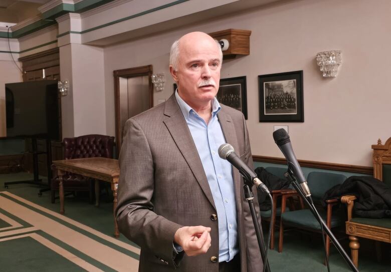 Man in brown suit standing in front of a microphone.