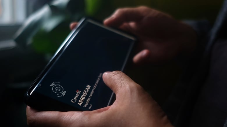 A person holds a smartphone set to the opening screen of the ArriveCan app.