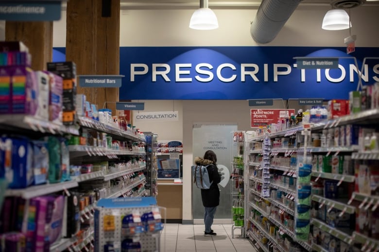 A person in winter clothing stands in an aisle at a Shoppers Drug Mart.