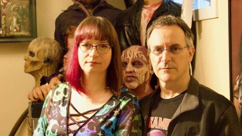 A portrait of two people posing in front of horrific models of human heads.