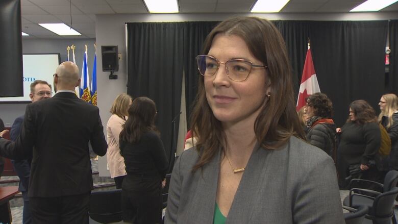 A woman wearing glasses stands in a crowded room.