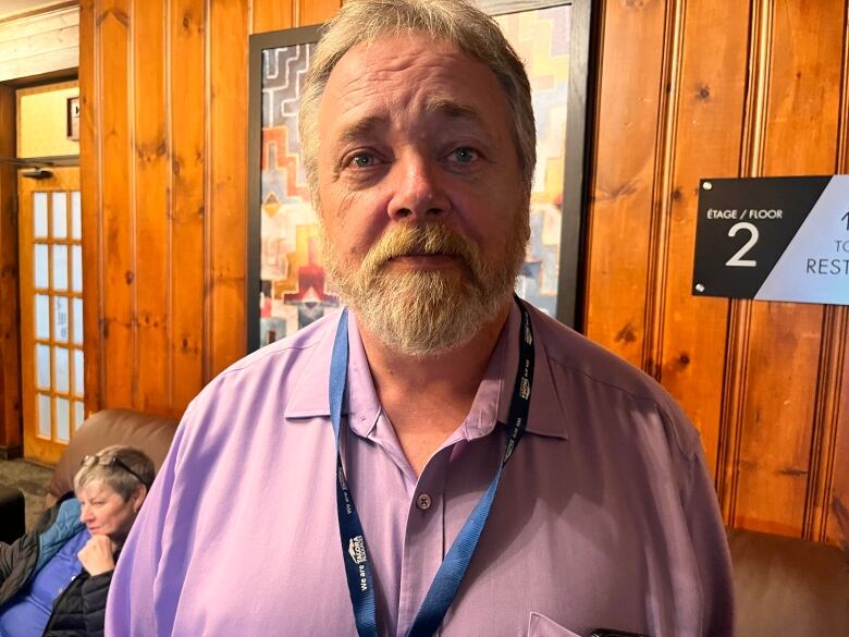 A man wearing a pink dress shirt stands in a hotel lobby.