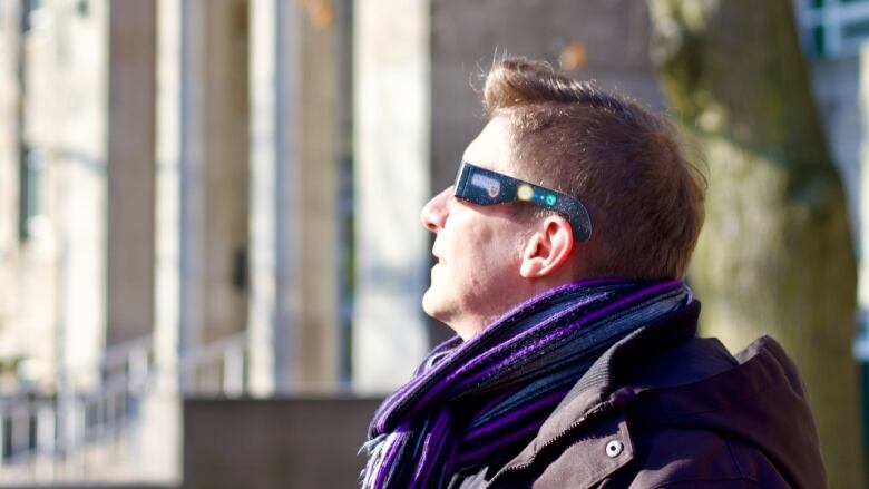 A person in paper eclipse glasses looks up at the sun. 