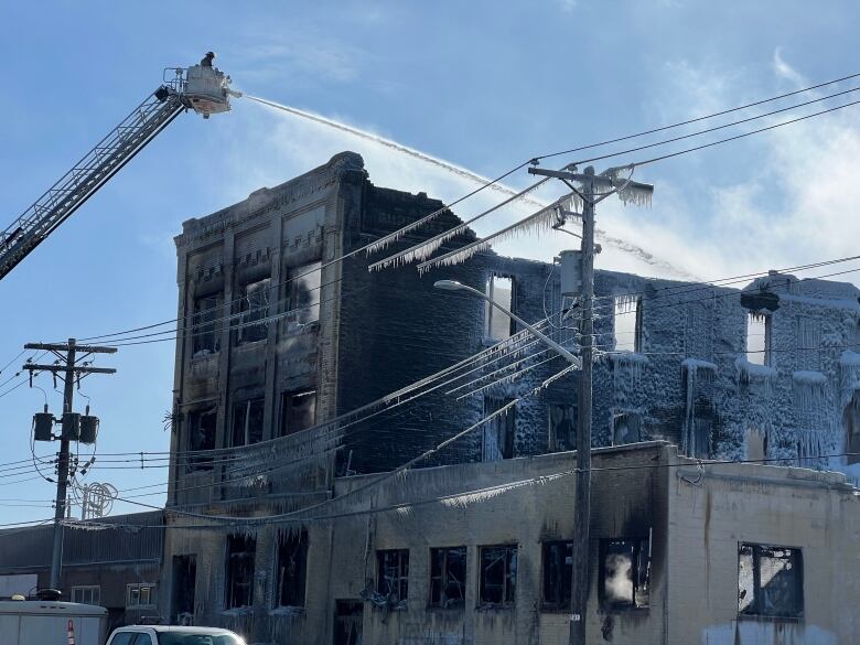 A crane sprays water on a fire damaged two-story building. 