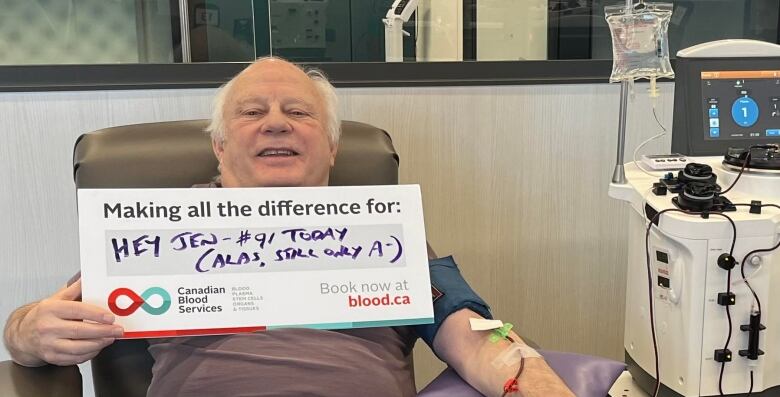 A man donating blood holding a sign. 