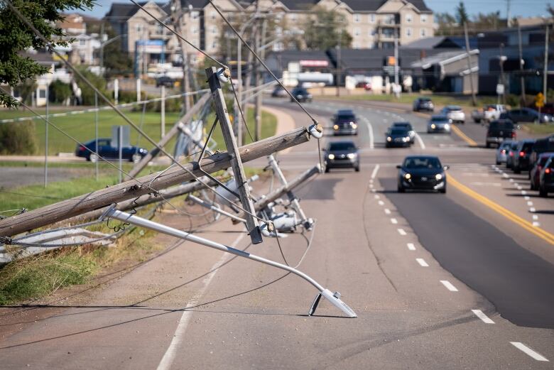 A utility pole lies across the road in Charlottetown as cars move around it. 