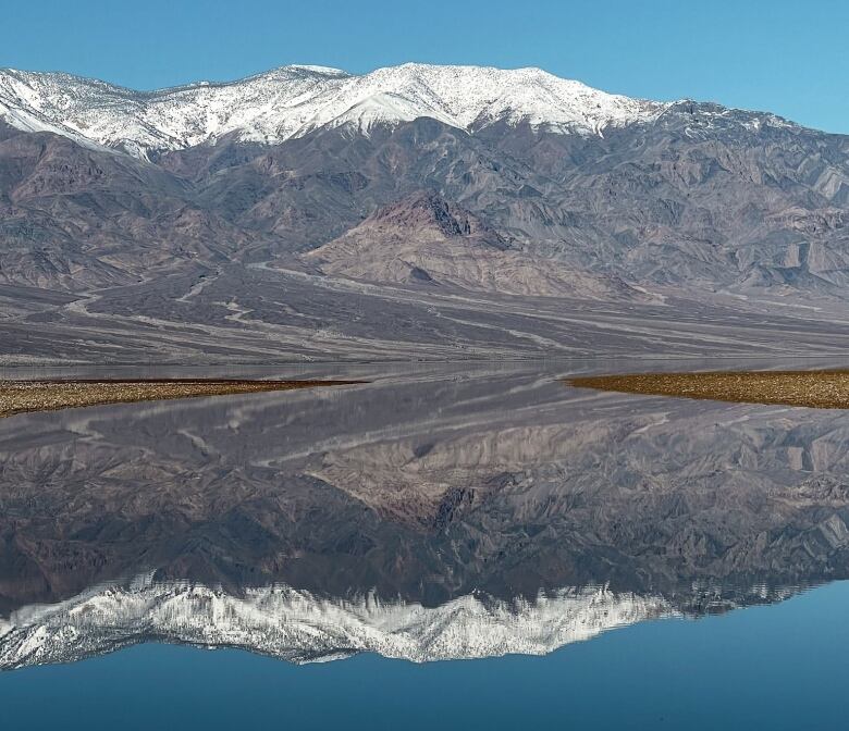 Snow-capped mountains are reflected in a lake.