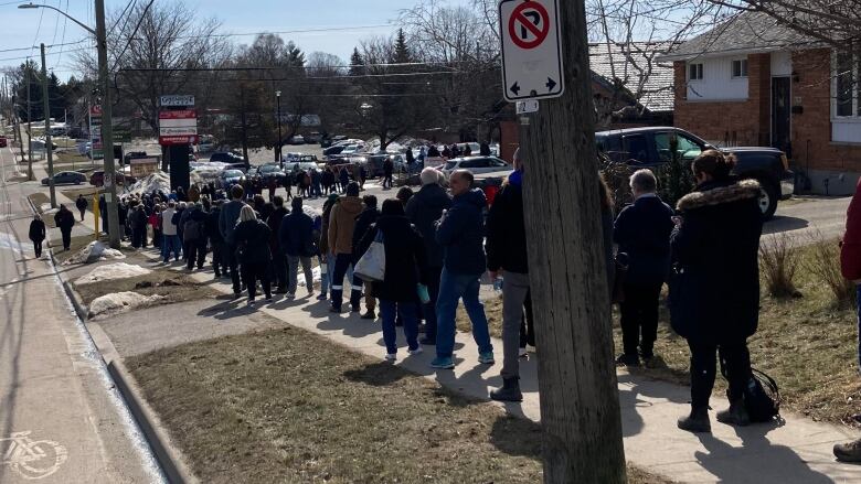 A people lining up outside on a sidewalk. 