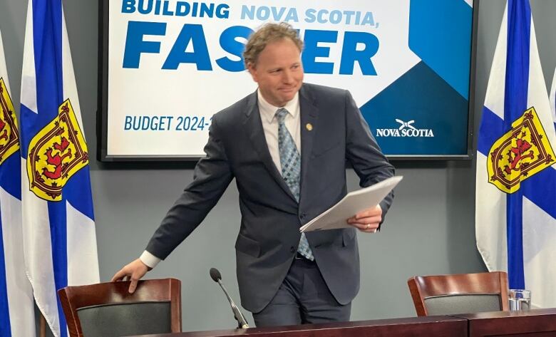 The finance minister prepares to take a seat at a news conference in front of a Nova Scotia provincial flag.