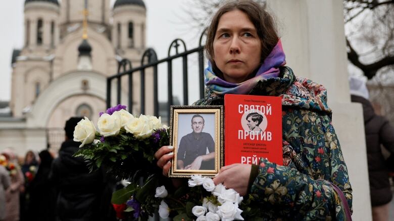 A woman flowers and a portrait of Alexei Navalny outside the church where a funeral service is held for him.