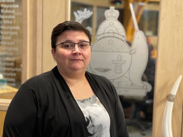 A woman poses in front of a door bearing the coat of arms for Nunavut. 