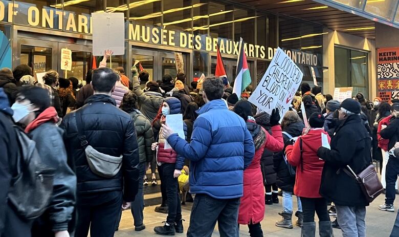 People carry signs and flags during a protest outside a building.