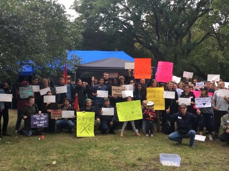 A group of workers stand in front of a tent holding signs.