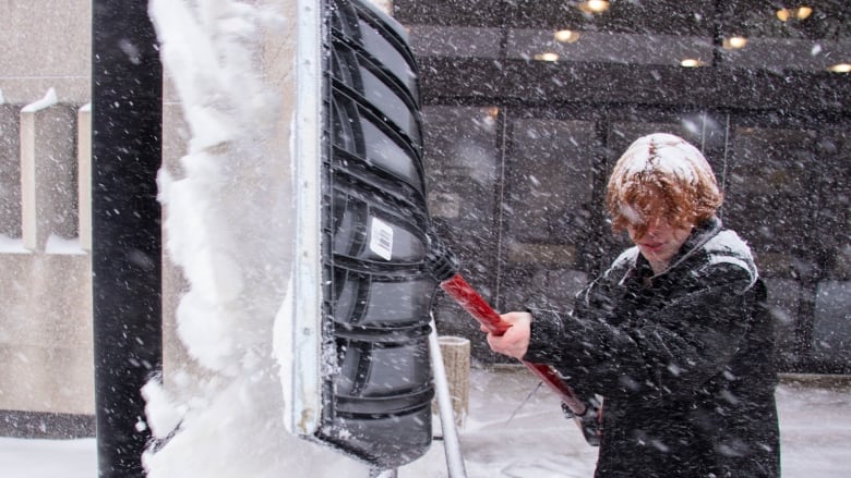 A person with their hair covered in snow shoveling snow.