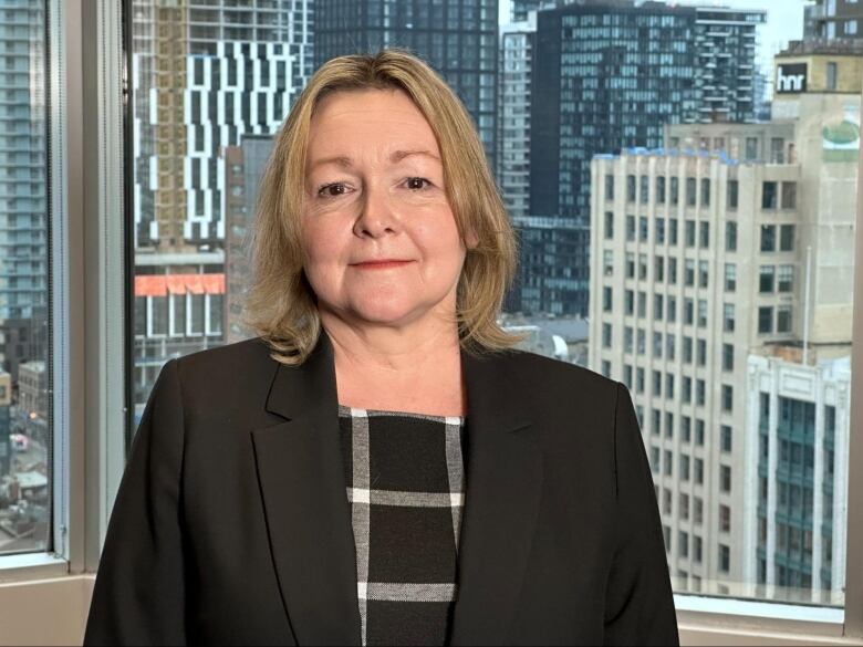 A woman in a blazer looks into the camera.