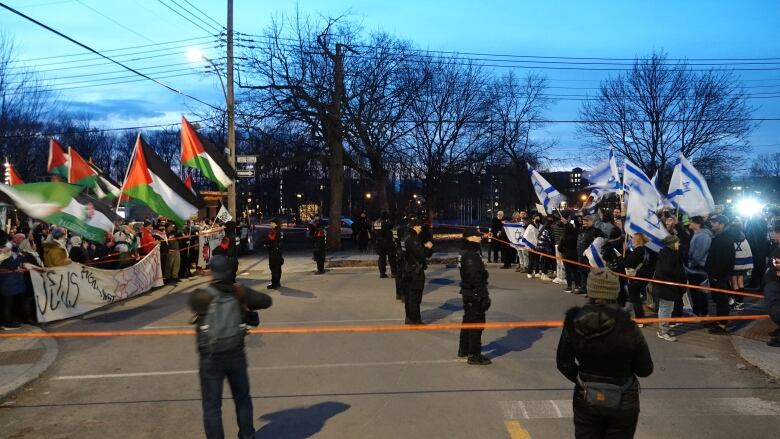 Two groups of protesters demonstrate outside a Montreal synagogue separated by police tape and officers.