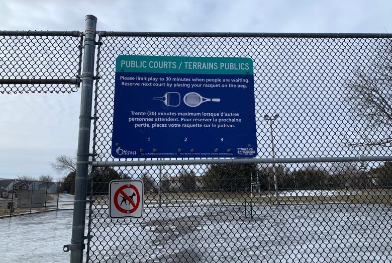 The tennis courts, covered in a sheet of ice, sit behind a fence with a sign that says 'Public Courts.'