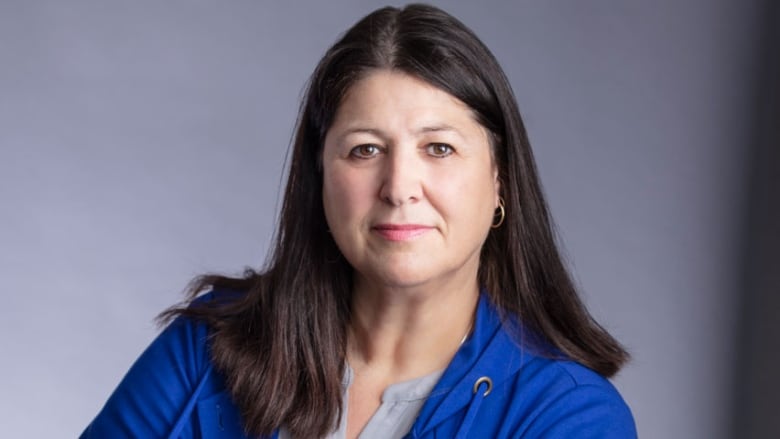 A portrait of a woman with shoulder-length brown hair, wearing a grey blouse and royal blue jacket.