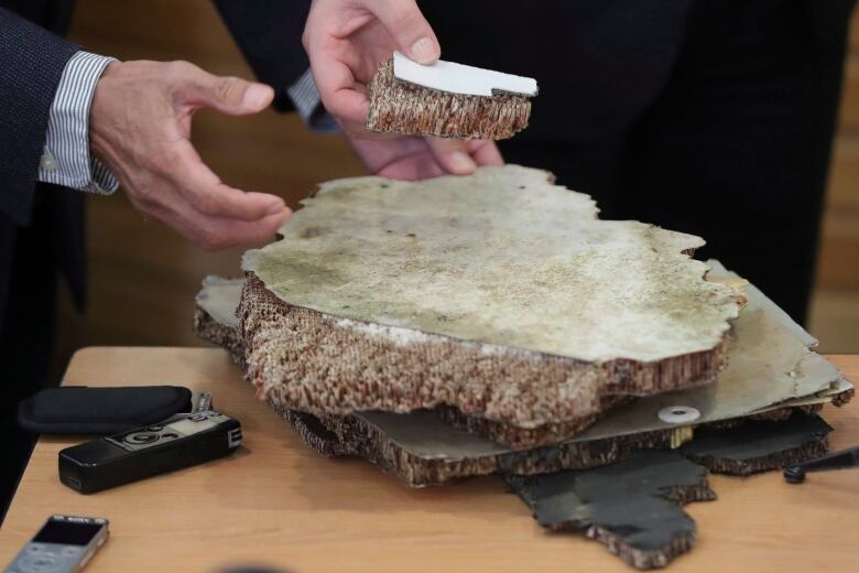 Hands pick up pieces of debris on a table. 