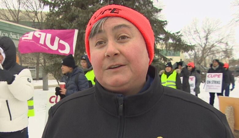 A woman is pictured speaking with a group of striking workers gathered behind her.