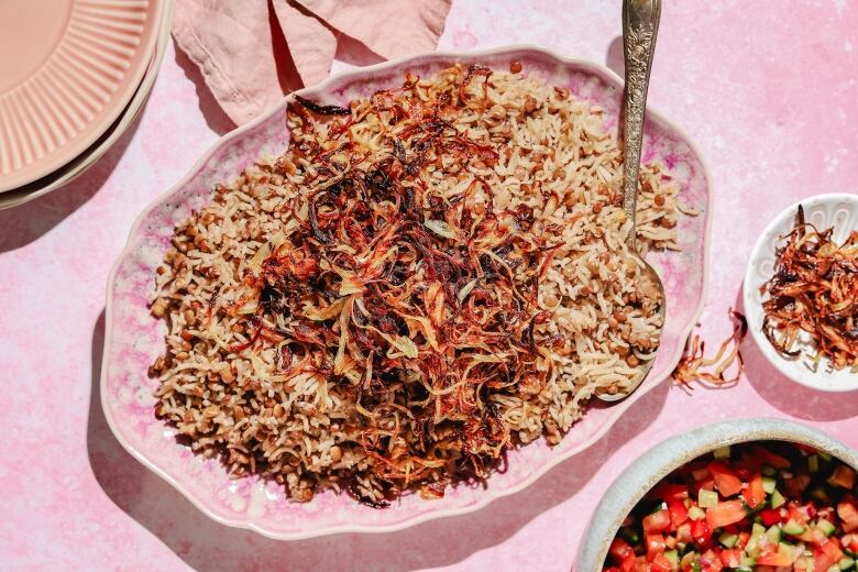 Overhead shot of a pink platter of mujaddara (cumin-spiced lentils, rice and crispy fried onions) on a pink table. 