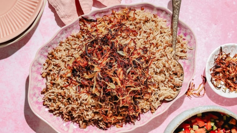 Overhead shot of a pink platter of mujaddara (cumin-spiced lentils, rice and crispy fried onions) on a pink table.