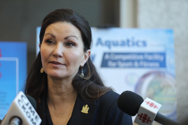 A woman in a black blazer stands in front of a posterboard with the word Aquatics on it. 