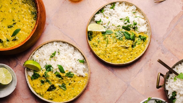 Overhead shot of 2 plates of zucchini dal with rice, sitting on a pink tiled surface. 