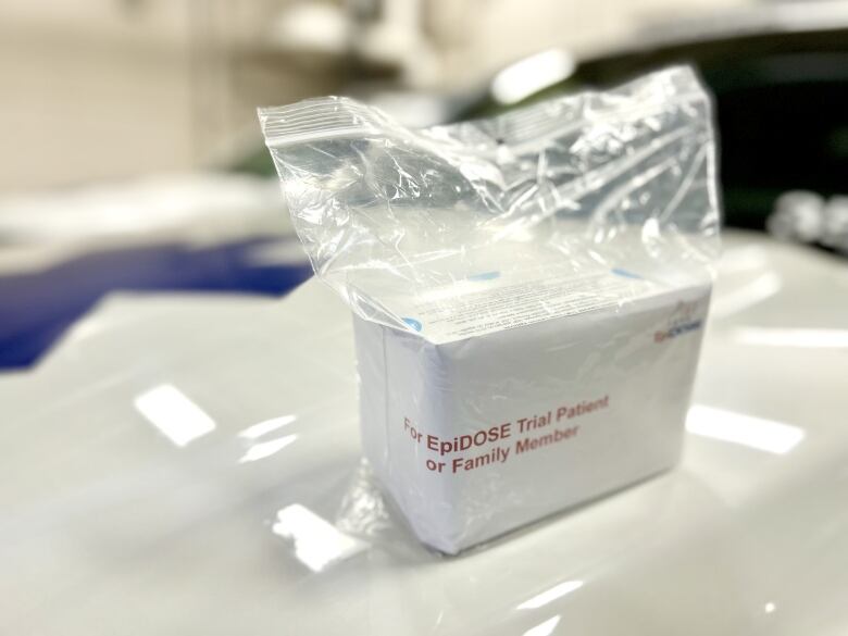 A white container sits in a plastic bag with red lettering that reads: 'For EpiDOSE Trial Patient or Family Member.'