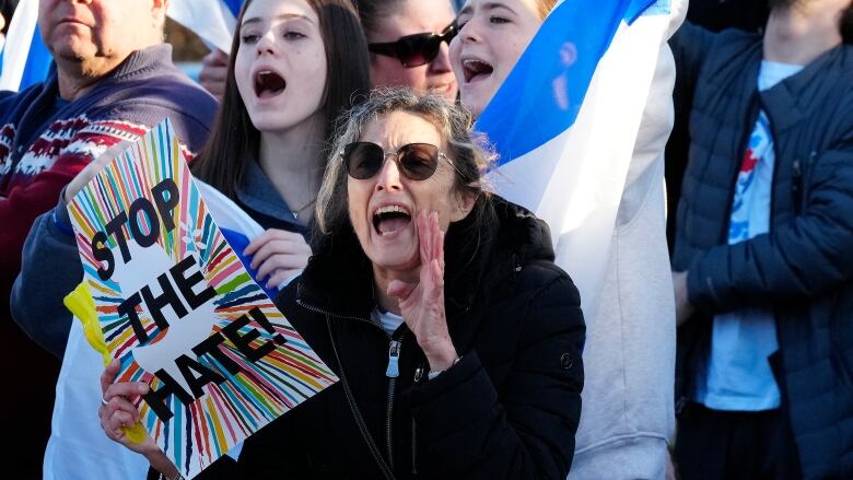 Protesters at an event. One of them holds a sign that says 