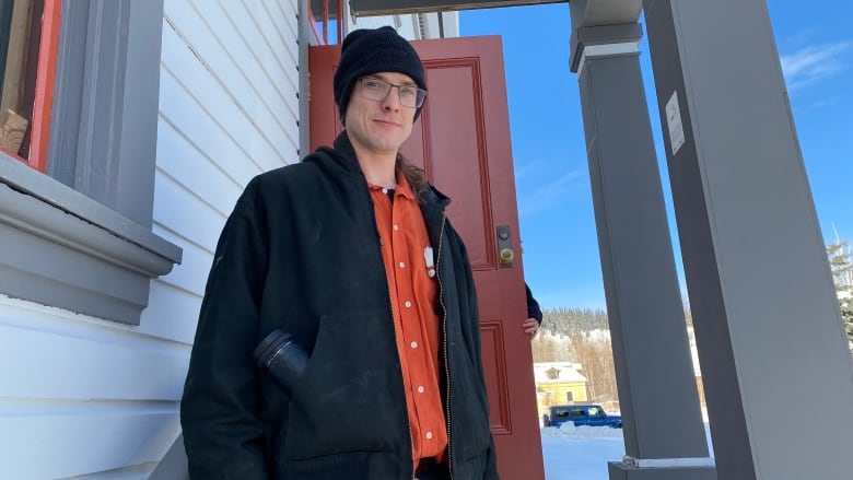 A man in a toque stands on some steps near the front entrance to a building.