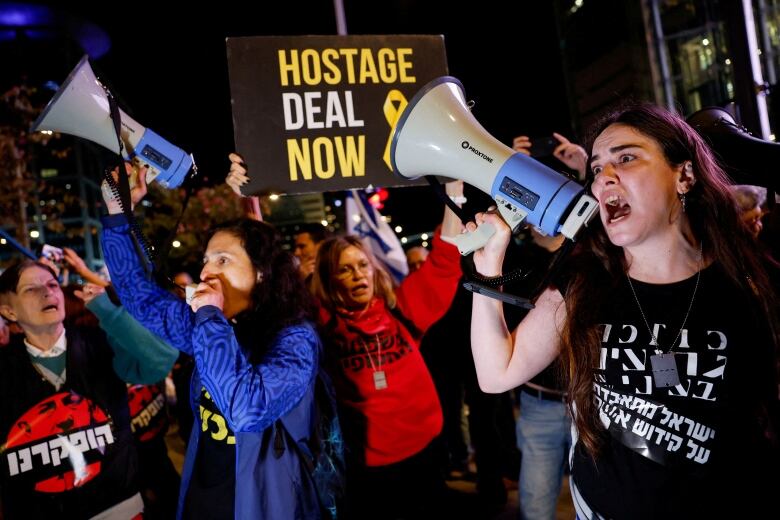 Demonstrators shout into megaphones while others hold up signs during a protest.