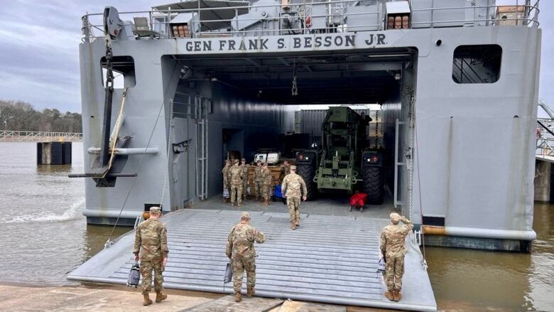 Soldier in uniform walk up a plank to a docked military vessel.