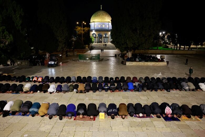 Worshipper pray in rows as a mosque is seen in the background.