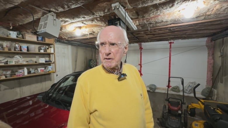 An elderly man in a yellow pullover looks off to his left.