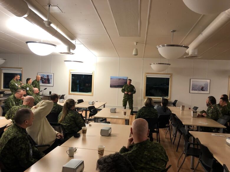 A man in a military uniform speaks with other military members.