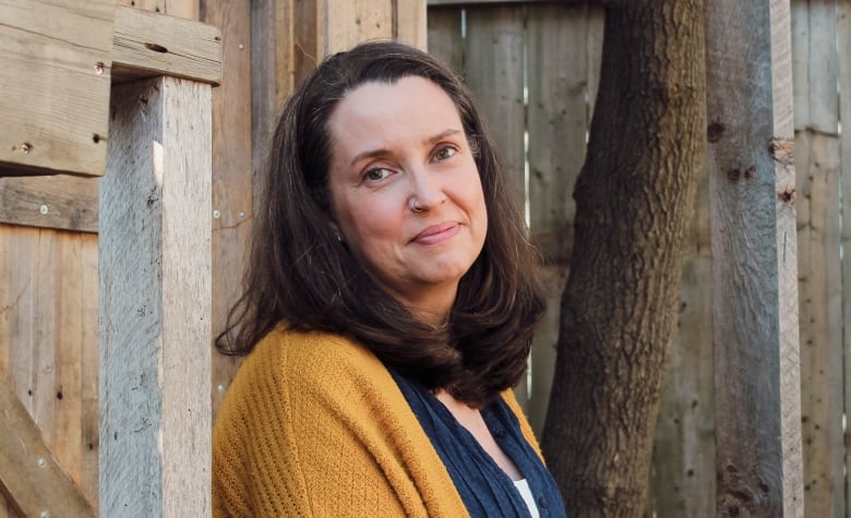 A portrait of a woman leaning against a wooden porch banister, slightly smiling at the camera. 