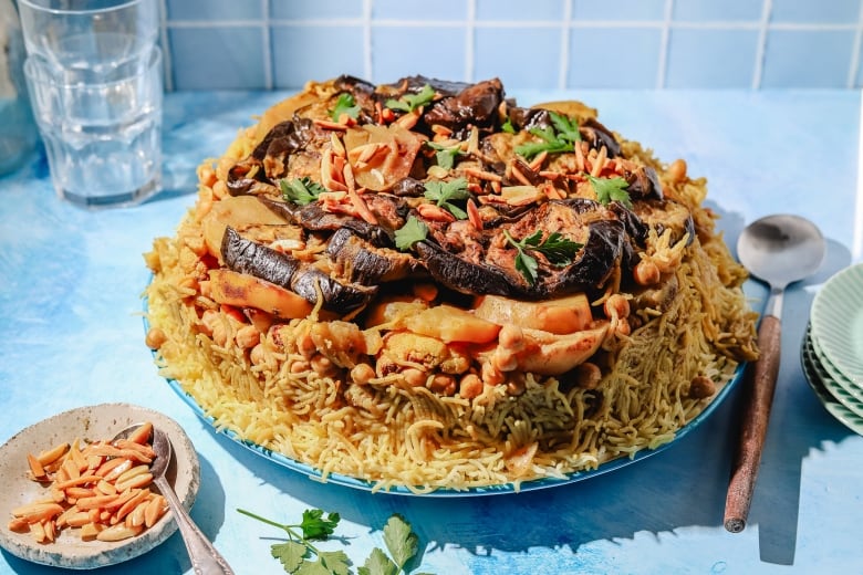 Maqluba (a rice dish with layers of eggplant, chickpeas and cauliflower on top) on a blue serving platter on a blue countertop. 