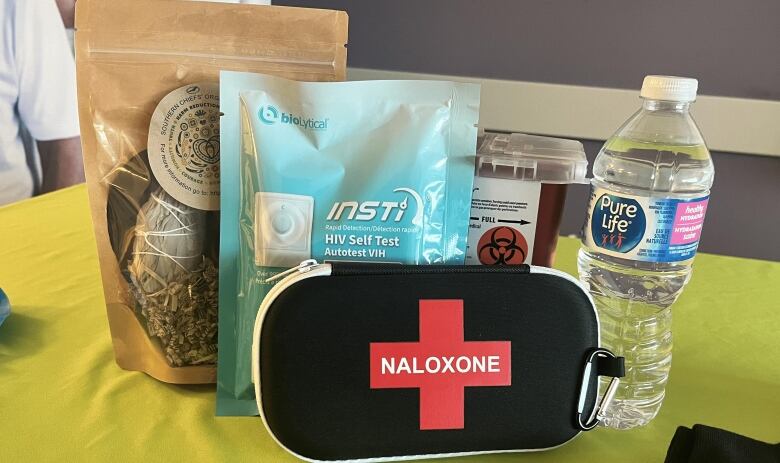 A package of sage, an HIV self-test, a naloxone kit, a sharps container and a plastic water bottle are pictured.