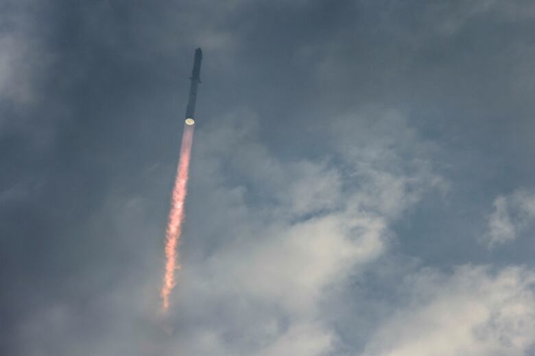 Exhaust flames shoot from the back of a rocket against a cloudy sky.