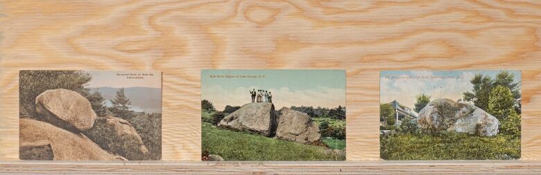 A row of three postcards on a wooden surface. The postcards are picture of boulders.