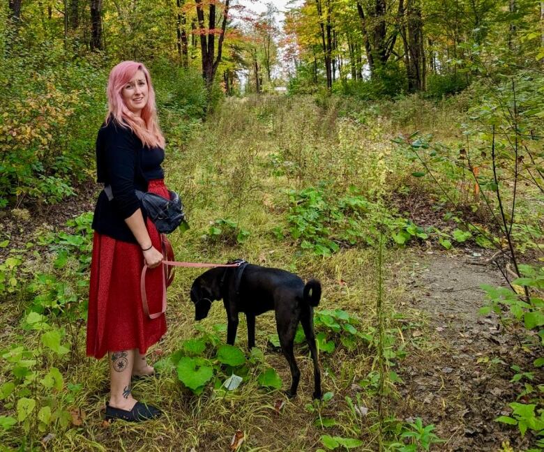 A woman stands with her dog in the woods.