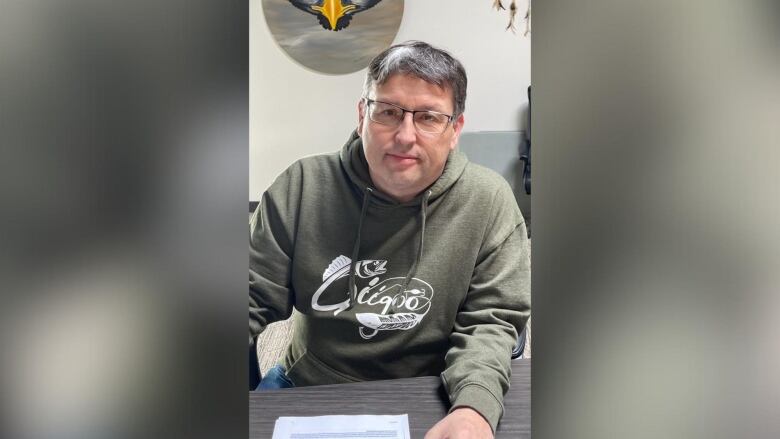 A person wearing a sage-green hoodie sits at a desk.