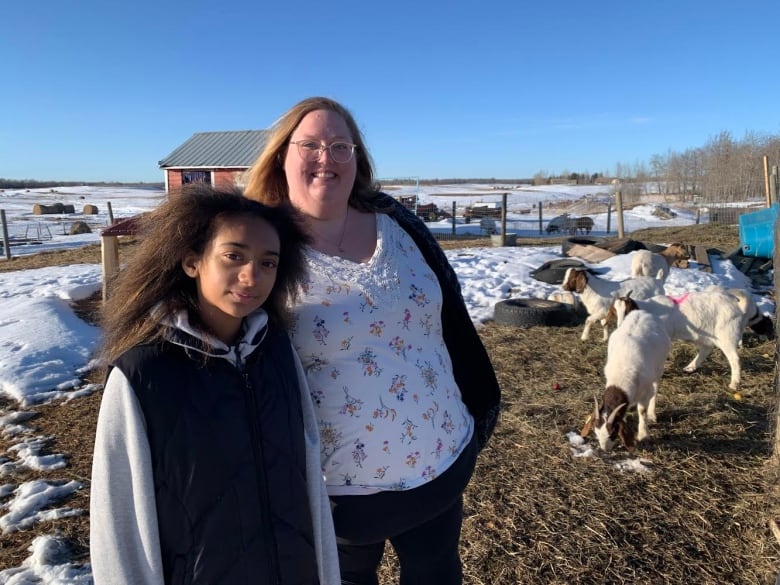 Two people stand near goats.