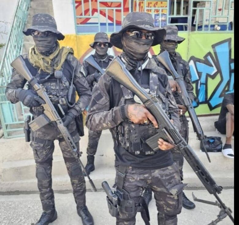 Gang members wearing paramilitary gear and carrying automatic weapons stand on a street in Port-au-Prince, Haiti.