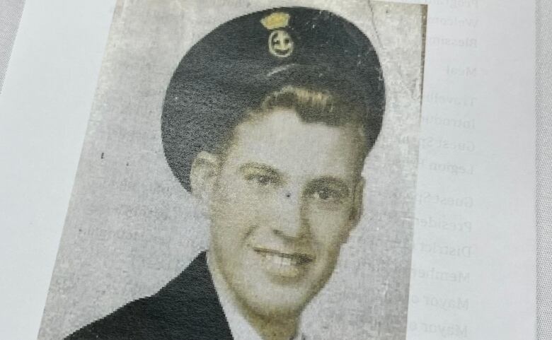 A black and white photo depicts a young man in a navy outfit.