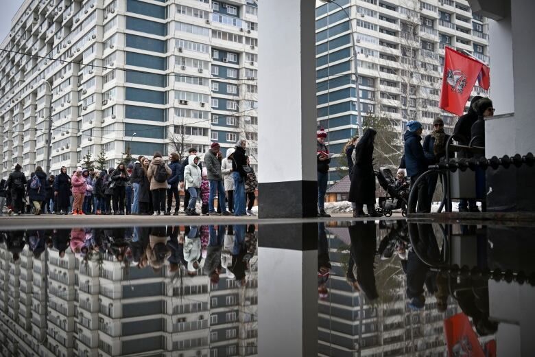 A puddle reflection shows people waiting in line.