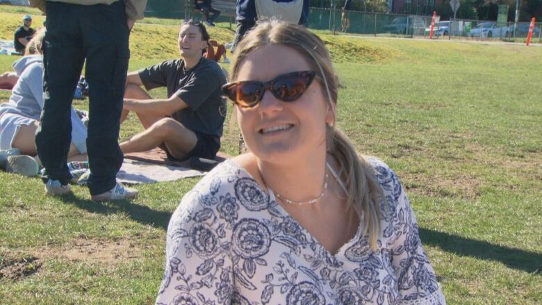 A woman in sunglasses sits on grass.