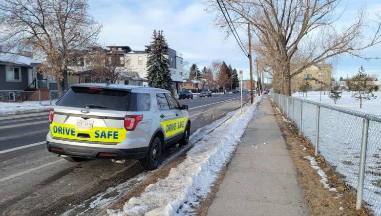 a silver SUV is parked alongside a snowy road. there are fluorescent yellow drive safe banners on the vehicle.